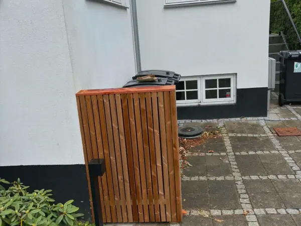 Affaldsskjuler i lodrette trælameller op ad hvid husmur